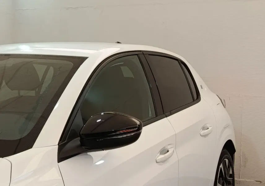 Vue latérale droite d'une Peugeot 208 électrique blanche avec rétroviseur noir et vitres teintées.