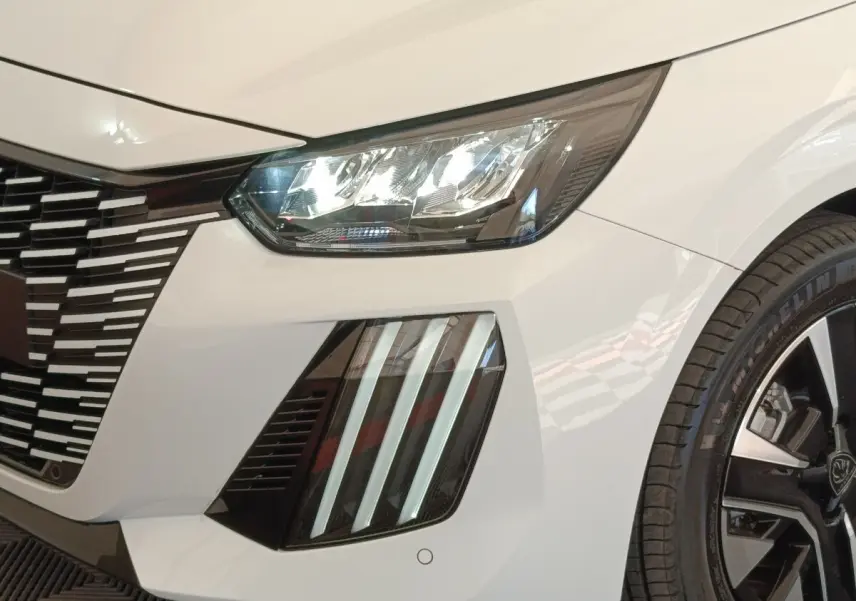 Gros plan avant droit du Peugeot 208 électrique blanc 2024, mettant en valeur les phares LED et la calandre distinctive.