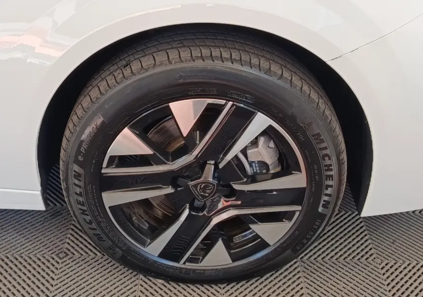 Gros plan sur la roue avant droite d’une Peugeot 208 électrique blanche avec jante alliage noire et argent.