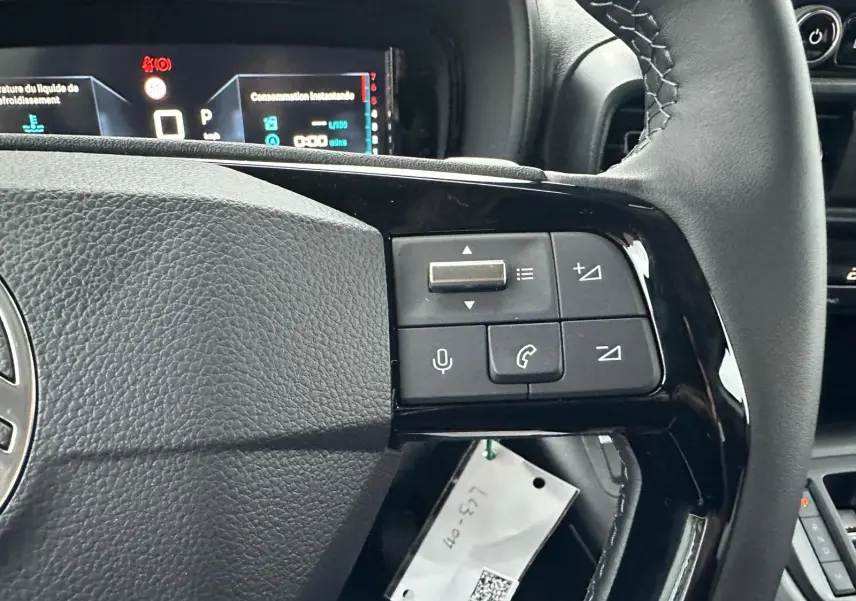 Gros plan sur les commandes au volant noir du Citroën Berlingo 2025, avec tableau de bord digital en arrière-plan.