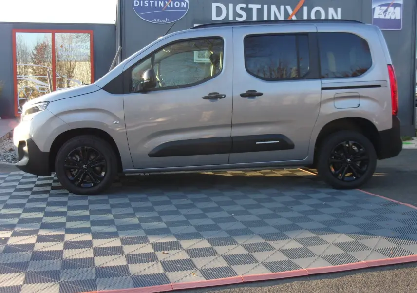 Vue de profil côté gauche d'un Citroën Berlingo gris Artense avec jantes noires, stationné devant une enseigne Distinxion.