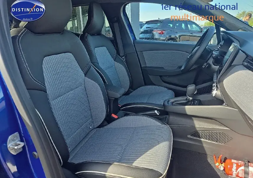 Intérieur avant de la Renault Clio V bleu iron, sièges sport gris et noir avec accoudoir central et tableau de bord visible.