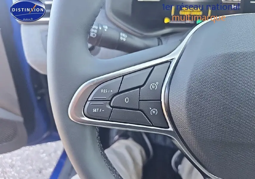 Gros plan sur les commandes au volant côté gauche d’une Renault Clio V Bleu Iron 2025 hybride essence.