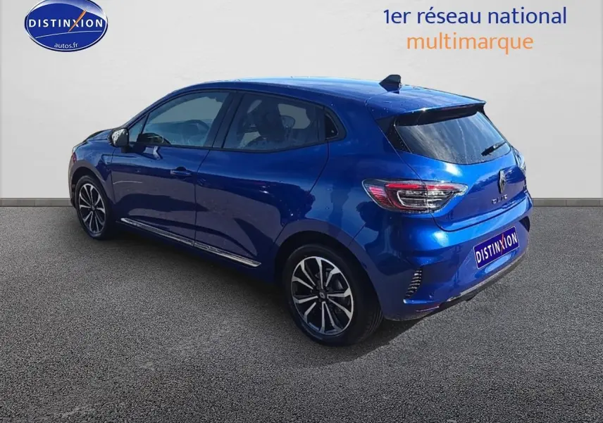 Renault Clio V bleu iron en 3/4 arrière droit, avec jantes alu et becquet arrière distinctif.