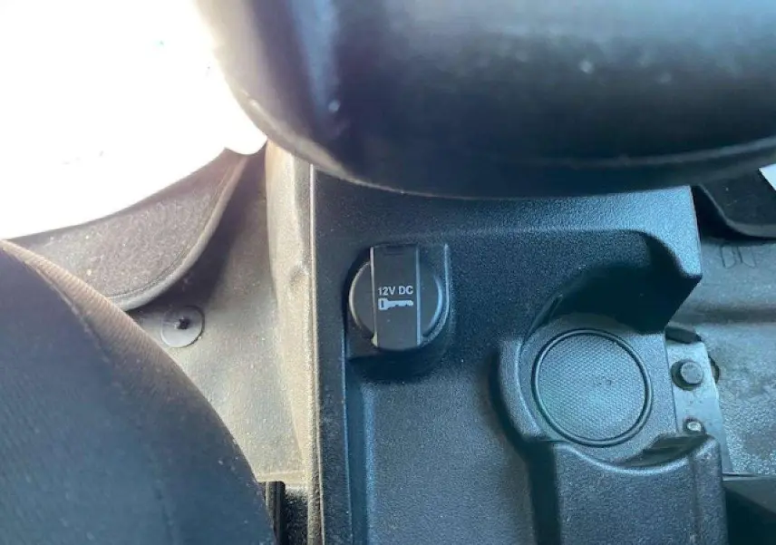 Prise 12V et porte-gobelet noir dans la console centrale du Fiat Doblo blanc, version fourgon 2017.