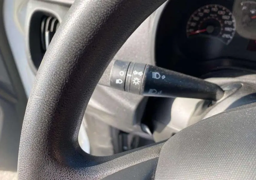 Gros plan sur le volant et la manette de clignotant du Fiat Doblo blanc, montrant le tableau de bord partiellement visible.