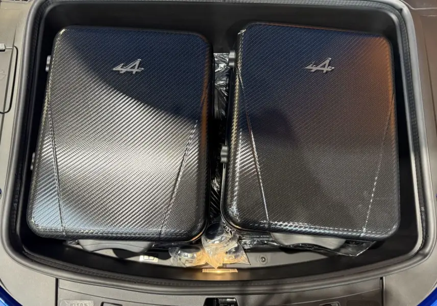 Vue plongeante sur le coffre avant bleu d'une Alpine A110 Legende 2019 avec deux valises carbone marquées du logo Alpine.