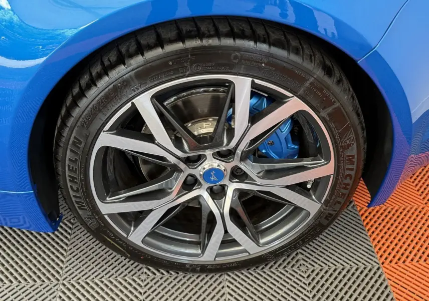 Gros plan sur la roue avant droite d'une Alpine A110 Legende bleu, avec étrier de frein bleu visible.