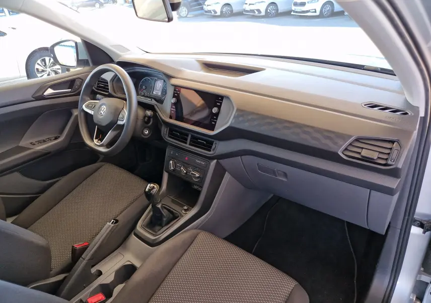 Vue intérieure côté conducteur du Volkswagen T-Cross 2019 argent métal, avec tableau de bord moderne et boîte manuelle.