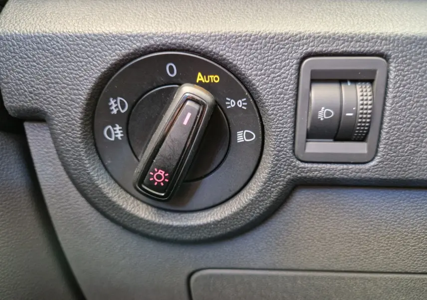 Gros plan sur le bouton de commande des phares du Volkswagen T-Cross argent métal, avec réglage automatique et molette d'intensité.