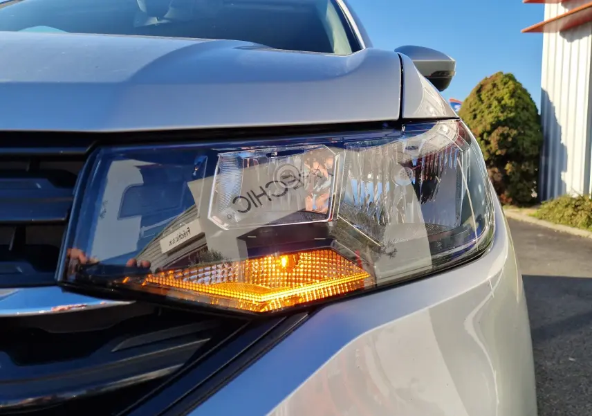 Gros plan sur le phare avant droit allumé d'un Volkswagen T-Cross argent métal 2019, sous un ciel bleu clair.