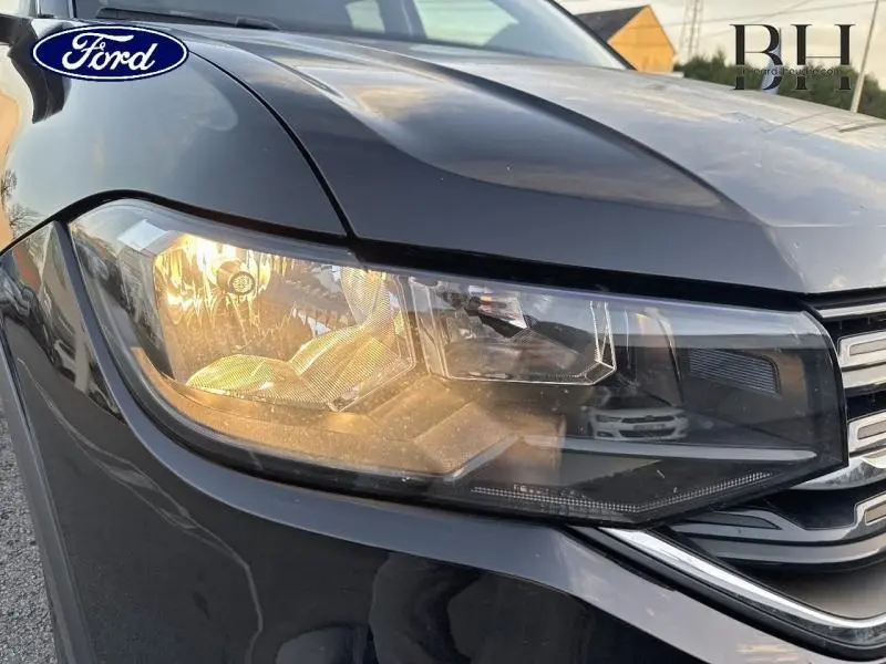 Gros plan sur le phare avant droit du Volkswagen T-Cross noir intense nacré, avec calandre partielle visible.