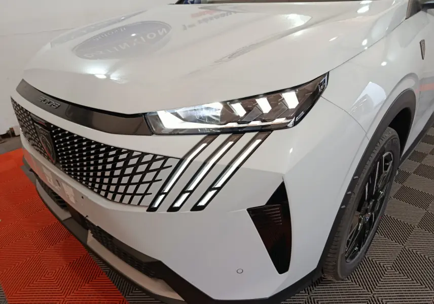 Vue 3/4 avant droit du Peugeot 3008 blanc hybride, mettant en valeur la calandre à motifs géométriques et les phares LED distinctifs.