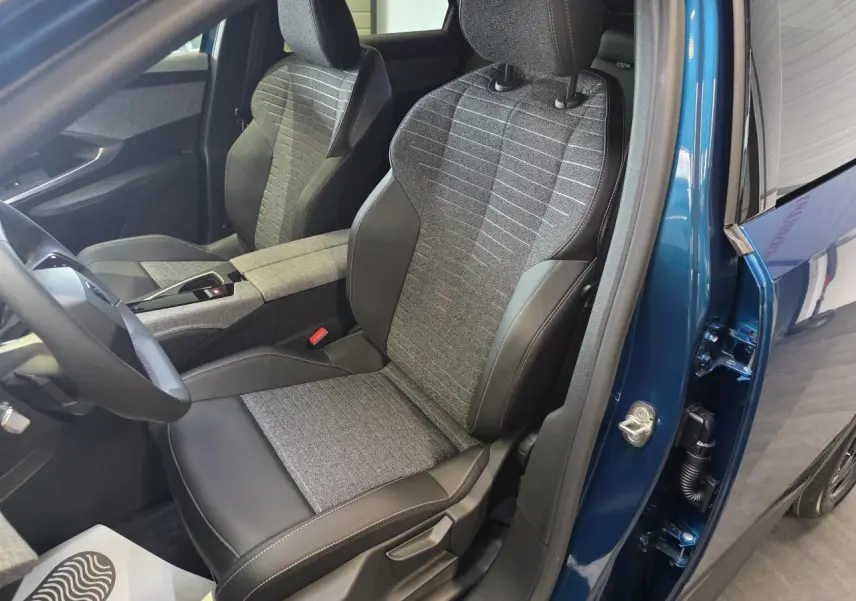 Vue intérieure côté conducteur du Peugeot 3008 bleu 2026, sièges tissu gris et cuir noir avec surpiqûres contrastées.