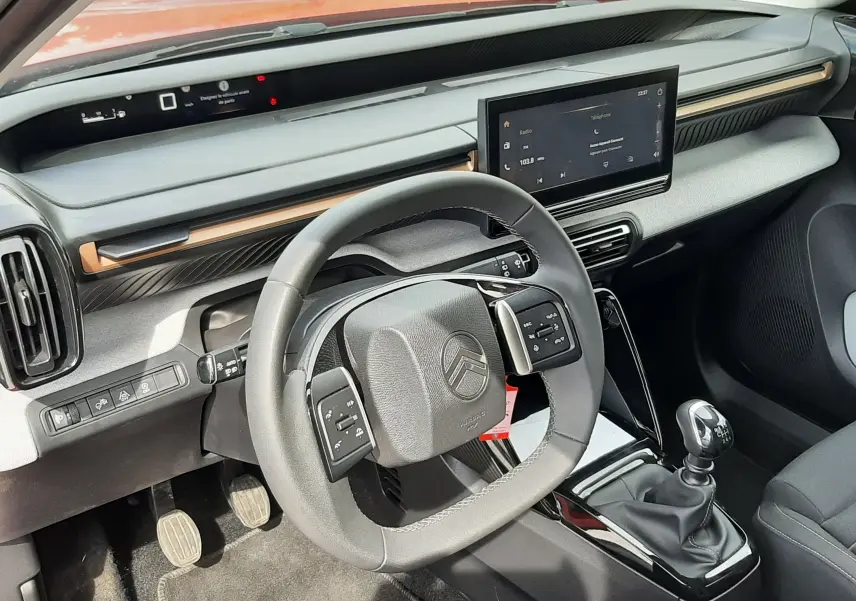 Vue intérieure côté conducteur du Citroën C3 Aircross 2025, tableau de bord gris noir avec volant multifonction et levier de vitesses manuel.