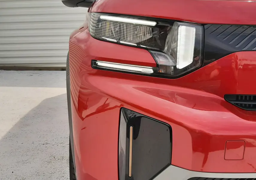 Gros plan sur l'avant gauche du Citroën C3 Aircross rouge Elixir avec toit noir, mettant en valeur son phare LED et sa calandre distinctive.