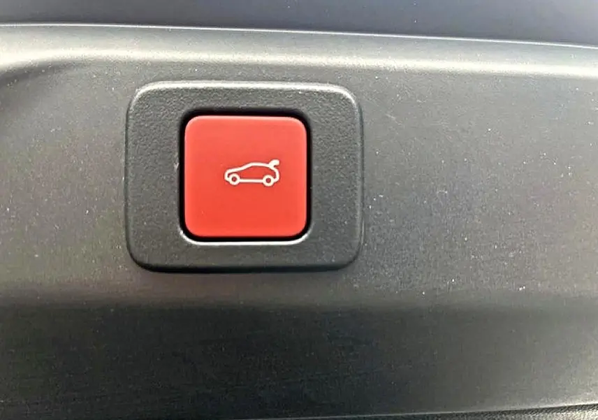 Bouton rouge d'ouverture électrique du coffre sur un Peugeot 3008 gris titane, vue en gros plan.