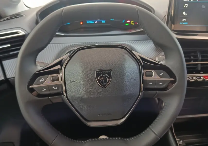 Vue rapprochée du volant cuir multifonctions de la Peugeot 208 électrique 2024 avec tableau de bord numérique en arrière-plan.