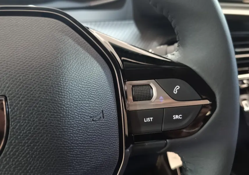 Gros plan sur les commandes multifonctions du volant cuir côté droit du Peugeot 208 électrique gris clair 2024.