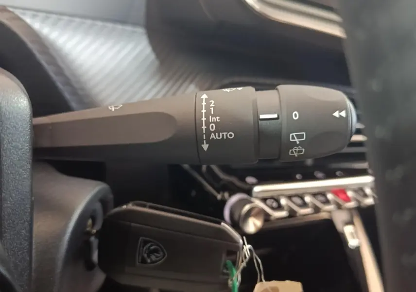 Gros plan sur la commande d’essuie-glace et clé de contact dans l’habitacle noir d’une Peugeot 208 électrique gris clair.