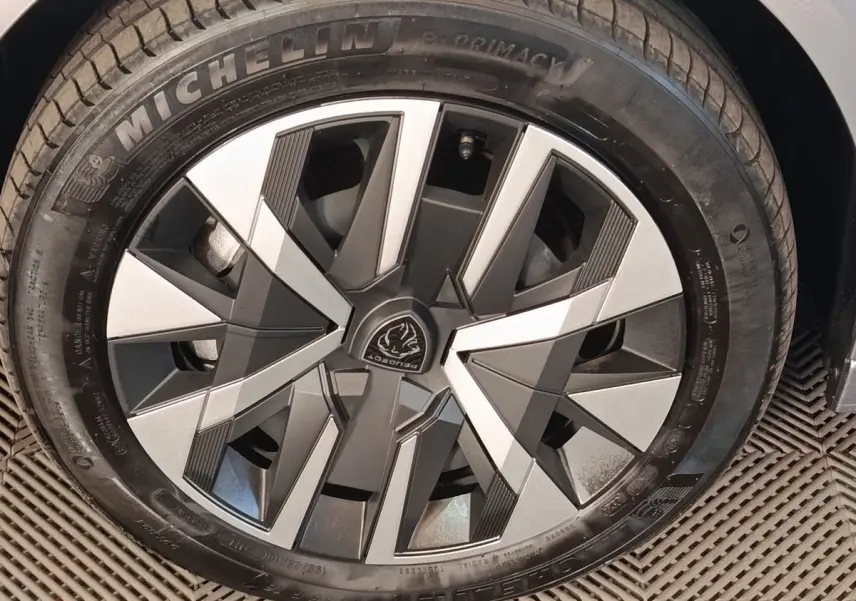 Gros plan sur la roue avant droite de la Peugeot 208 électrique 2024 gris clair avec jante au design géométrique bicolore.
