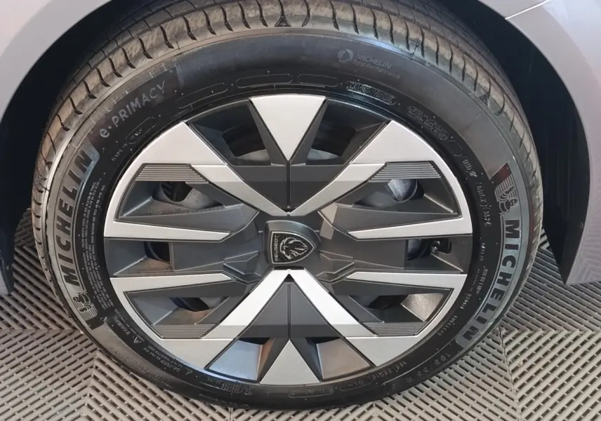Gros plan sur la roue avant droite gris clair du Peugeot 208 électrique 2024 avec jante au design géométrique noir et argent.