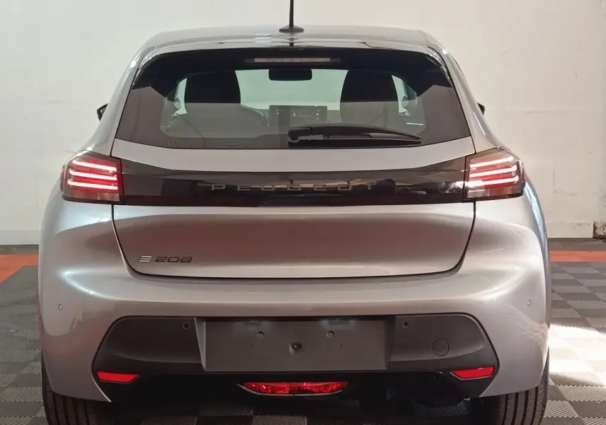 Vue arrière d'une Peugeot 208 électrique gris clair 2024 avec feux LED allumés et logo PEUGEOT central.