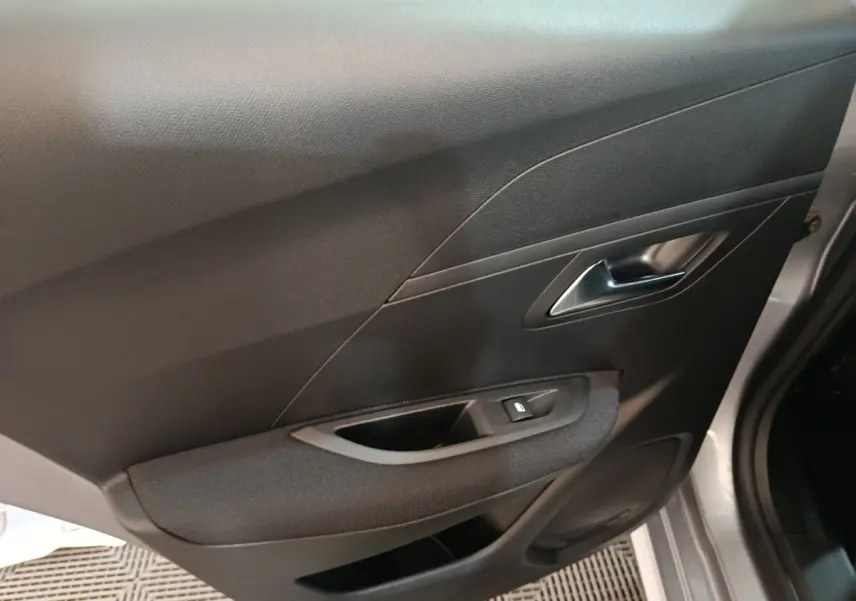 Vue intérieure côté droit de la porte d’une Peugeot 208 électrique 2024 gris clair avec poignée argentée et bouton de vitre.