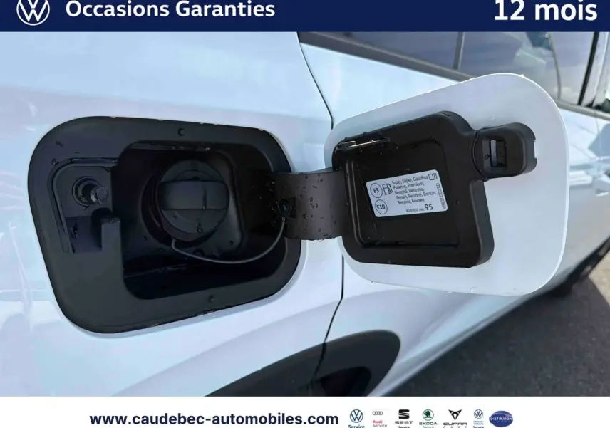 Gros plan sur la trappe à carburant ouverte côté gauche d’un Volkswagen T-Roc blanc, avec bouchon essence visible.