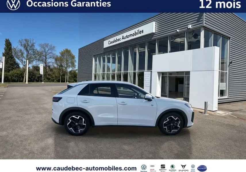 Volkswagen T-Roc blanc vue de profil côté gauche, avec jantes alliage noires et bâtiment Caudebec Automobiles en arrière-plan.