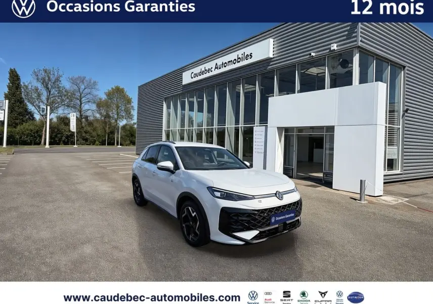 Volkswagen T-Roc blanc vue 3/4 avant droit, avec jantes noires et logo lumineux, devant un bâtiment moderne.