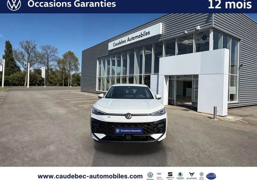 Vue avant d'un Volkswagen T-Roc blanc garé devant un bâtiment moderne avec logo VW lumineux sur la calandre.