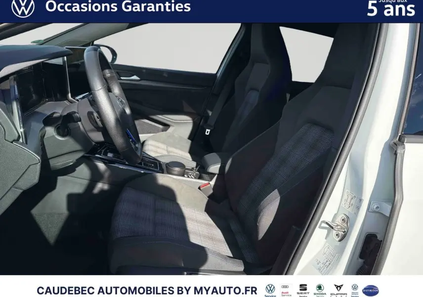 Vue intérieure côté conducteur d'une Volkswagen Golf 1.5 eHybrid blanche, sièges sport à motifs et volant multifonction cuir.
