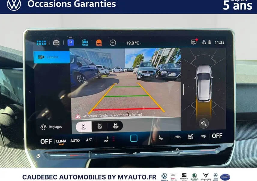 Écran tactile intérieur affichant la caméra de recul et l'aide au stationnement d'une Volkswagen Golf blanche, vue du tableau de bord.