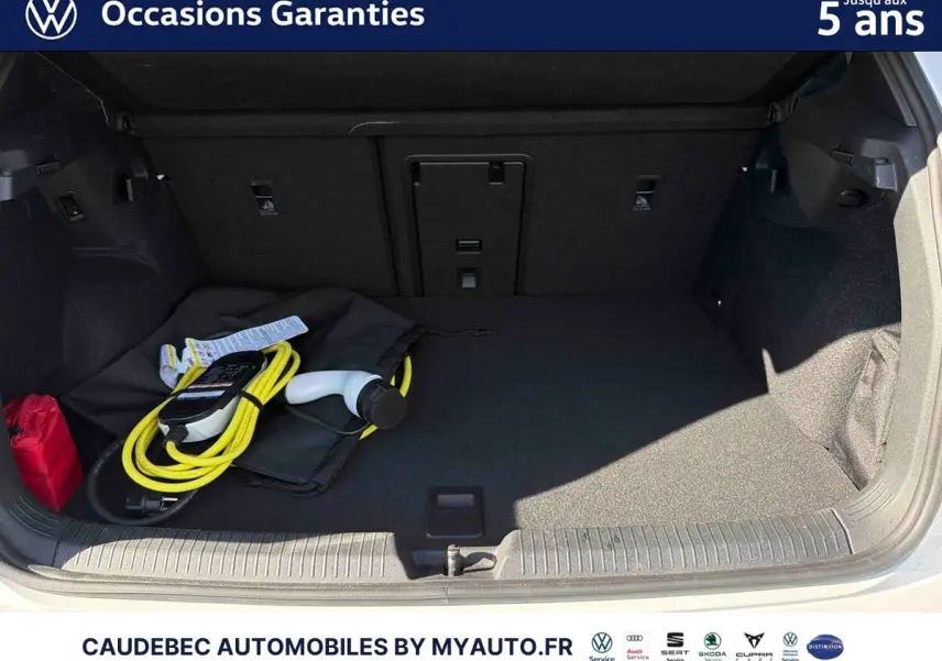 Coffre ouvert d’une Volkswagen Golf 1.5 eHybrid blanche avec câble de recharge électrique visible.