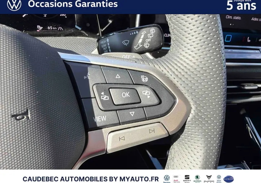 Gros plan sur les commandes multifonctions du volant en cuir perforé gris clair d'une Volkswagen Golf blanche.