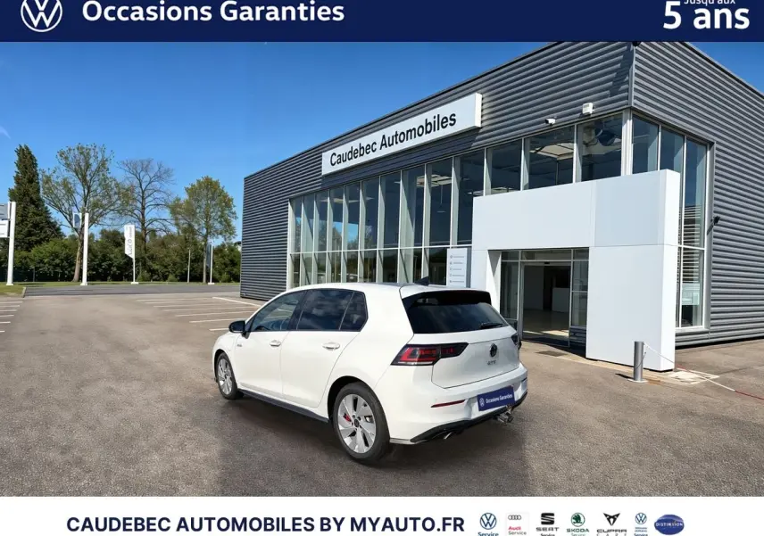 Vue 3/4 arrière droite d'une Volkswagen Golf 1.5 eHybrid blanche, avec attelage escamotable et vitres surteintées.