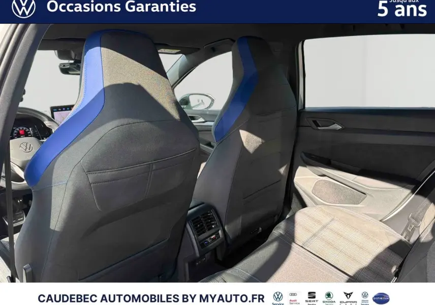 Vue intérieure arrière montrant les sièges avant noirs avec surpiqûres bleues et la banquette arrière grise à motifs de la Volkswagen Golf blanche.