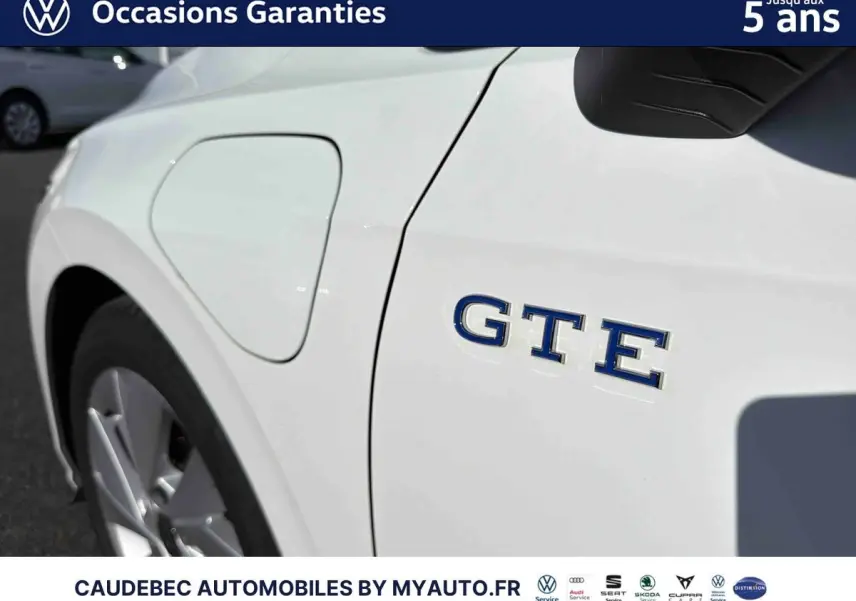 Gros plan sur l'aile avant gauche blanche d'une Volkswagen Golf 1.5 eHybrid avec logo GTE bleu visible.