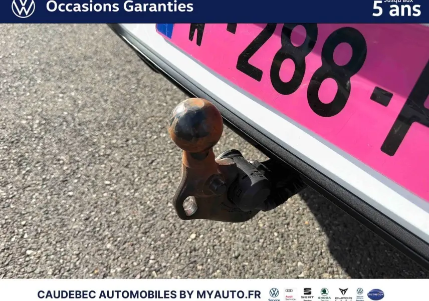 Gros plan sur l'attelage escamotable électrique à l'arrière d'une Volkswagen Golf blanche, avec plaque d'immatriculation rose.