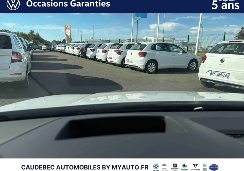 Vue depuis l'intérieur vers l'avant d'une Volkswagen Golf blanche stationnée dans un parking extérieur.