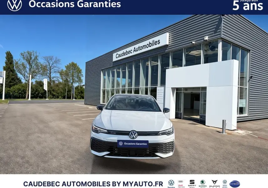 Vue frontale d'une Volkswagen Golf 1.5 eHybrid 272 DSG6 blanche, devant un bâtiment moderne de concession automobile.