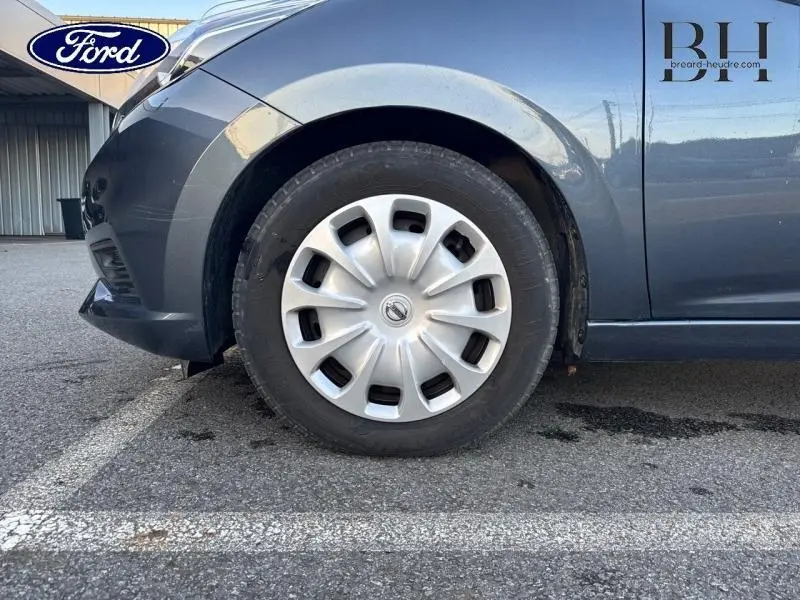 Gros plan sur la roue avant gauche grise acier d'une Nissan Micra 2018 avec enjoliveur et partie basse du bouclier avant.