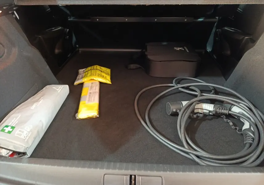 Coffre ouvert vu de face d'une Peugeot 208 électrique blanche de 2020 avec câble de recharge et trousse de secours.