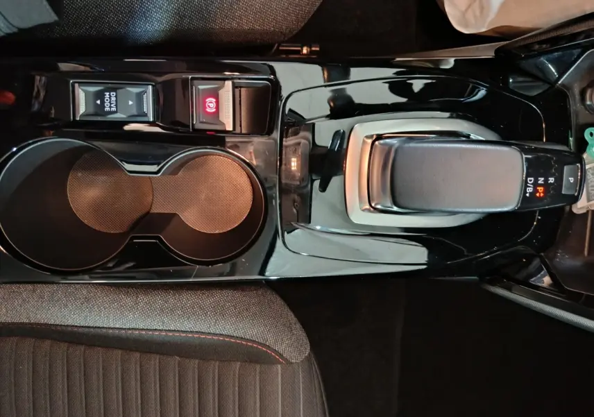 Vue plongeante sur la console centrale noire de la Peugeot 208 électrique avec levier de vitesses et boutons Drive Mode et frein à main.