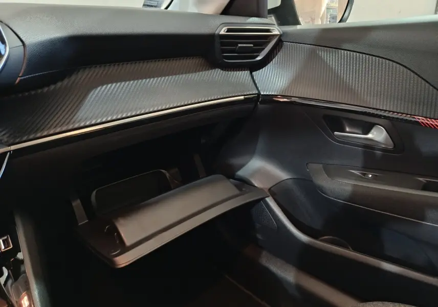 Vue intérieure côté passager du tableau de bord et boîte à gants ouverte d'une Peugeot 208 électrique blanche de 2020.