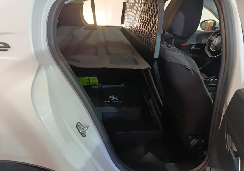 Vue intérieure côté gauche arrière d’une Peugeot 208 électrique blanche, avec siège avant et filet de protection visible.