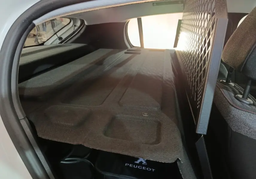 Vue intérieure du coffre arrière d'une Peugeot 208 électrique blanche, avec séparation grillagée et banquette rabattue.
