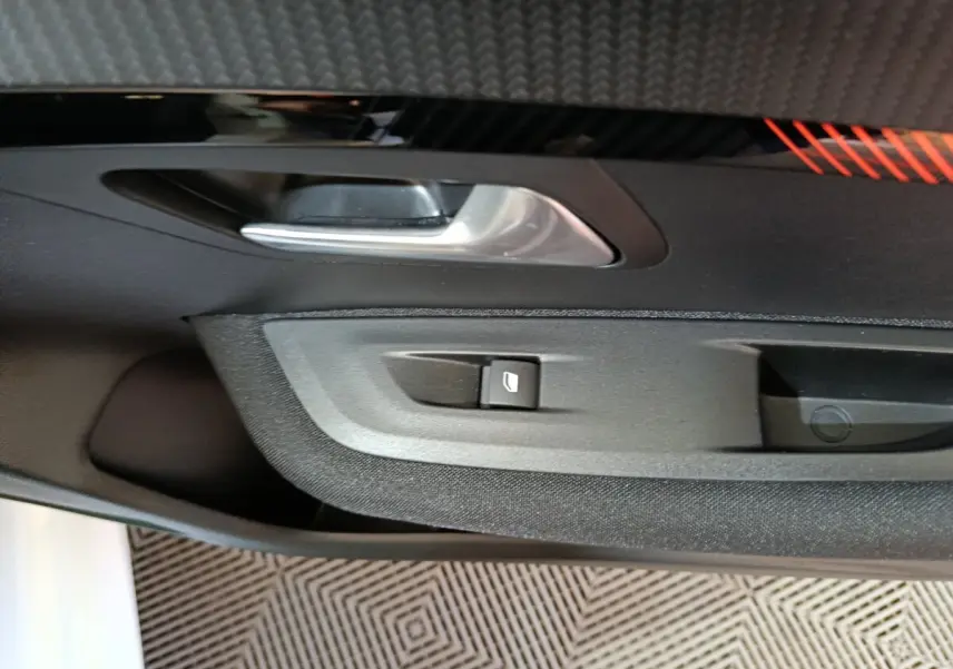 Gros plan sur la poignée intérieure et le bouton de lève-vitre côté gauche d’une Peugeot 208 électrique blanche.