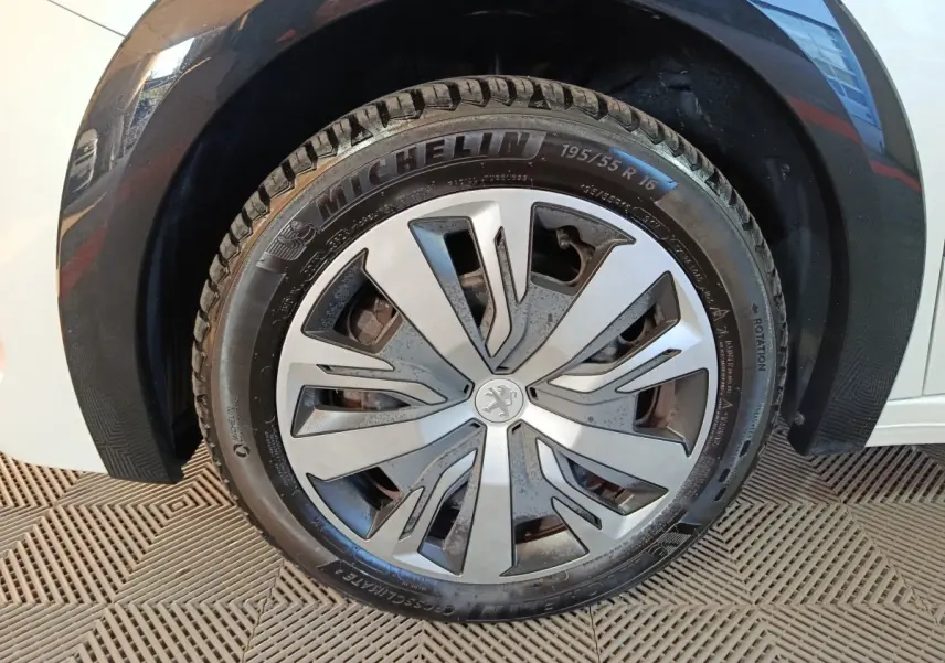 Gros plan sur la roue avant droite d'une Peugeot 208 électrique blanche, avec jante en alliage au design moderne.